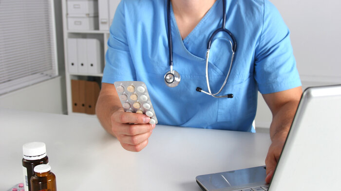 bildet viser en lege som holder et brett med piller i hånda