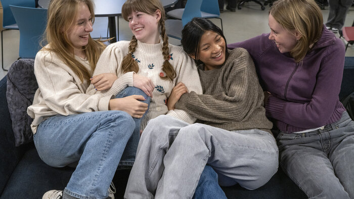 Bildet viser fire unge, blide jenter sammen i en sofa