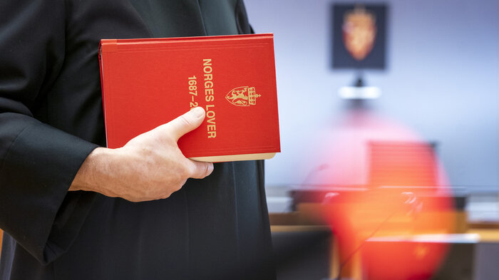 Bildet viser en dommer med Norges lover i hånden.