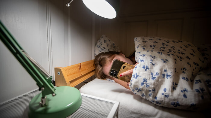 bilde av kvinne i sengen med mobil