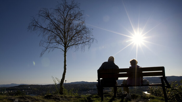Bildet viser to eldre mennesker som sitter på en benk i motlys