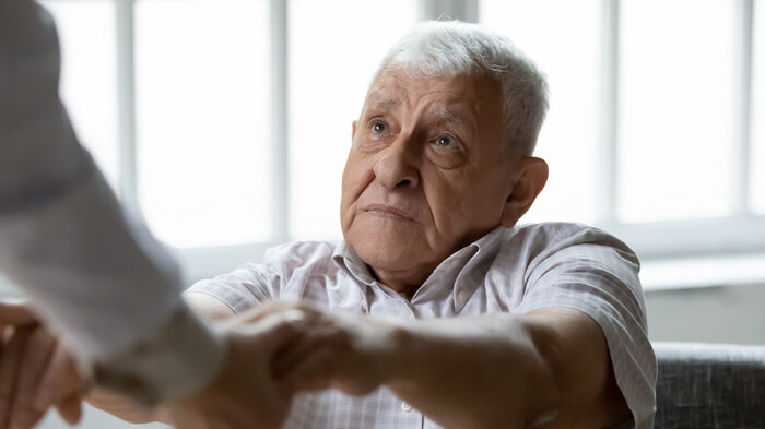 Bildet viser en eldre mann som holder hendene til noen utenfor bilderammen