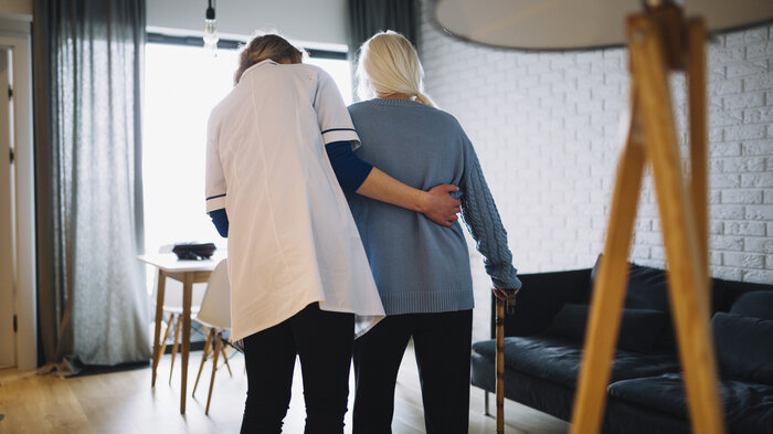 Bildet viser en pleier som støtter en eldre pasient