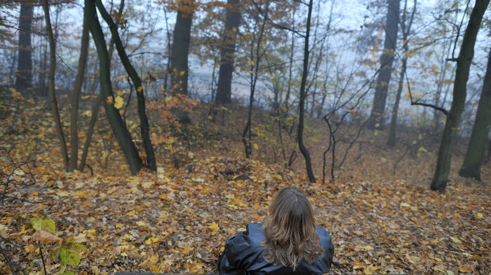 Bilde viser en dame som sitter på en benk med ryggen til
