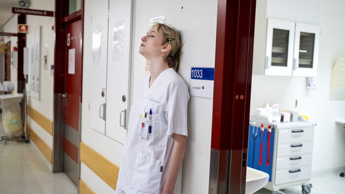 Bildet viser en sliten sykepleier som er lent mot veggen med ryggen.