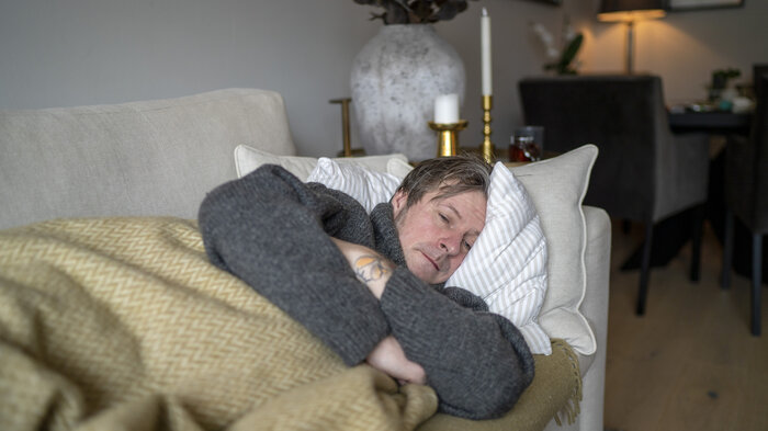 Bildet viser en mann som ligger på sofaen og er syk.