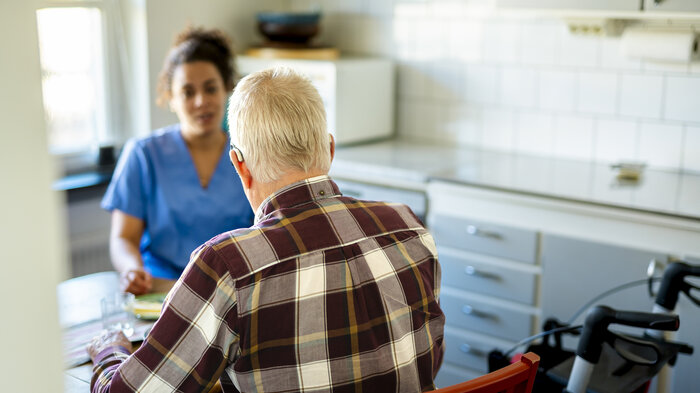 Bildet viser en mann som sitter med ryggen til kamera, vendt mot en pleier.