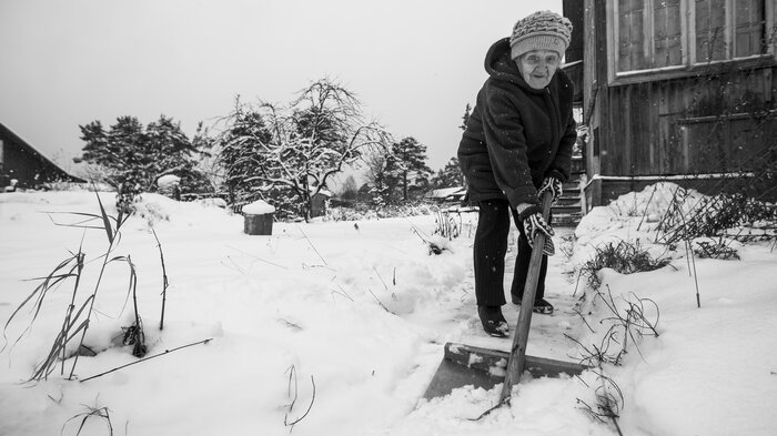 bildet viser eldre dame som måker snø