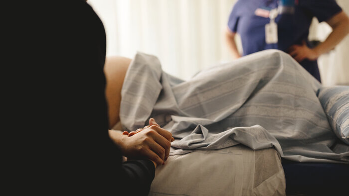 Bildet viser en kvinne som skal føde. I bakgrunnen: en jordmor.