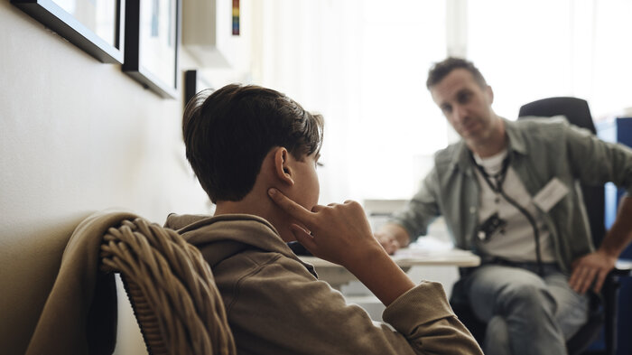 Bildet viser en helsesykepleier og en ung gutt som sitter på et kontor.