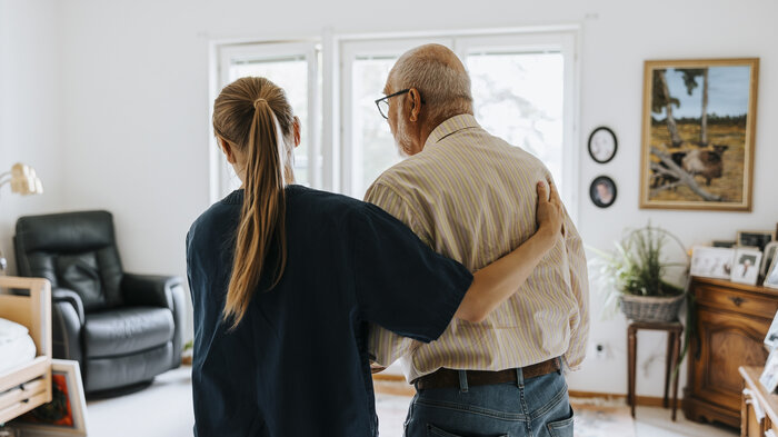 Bildet viser en sykepleier som støtter en eldre mann på sykehjem.
