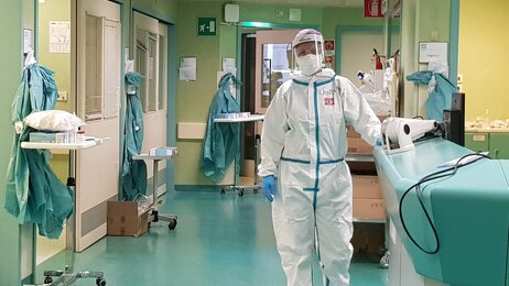 Bildet viser en sykepleier i smittevernutstyr i en sykehuskorridor.