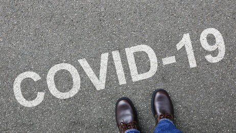 Bildet viser et menneske som ser ned på bakken hvor det står covid-19