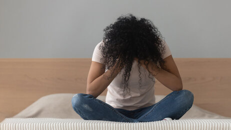 Bildet viser en kvinne som sitter alene på en seng med hodet i hendene