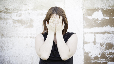 Bildet viser en kvinne som dekker ansiktet med hendene