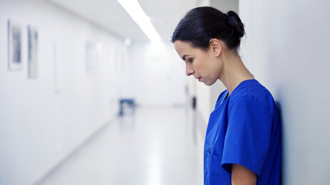 Bildet viser en sykepleier som står inntil en vegg. Hun er sliten