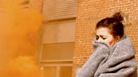 Bildet viser en skadet kvinne med et pledd rundt seg. Det er røykskyer rundt henne.