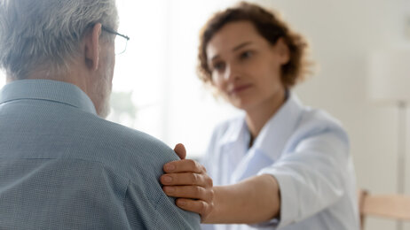 Bildet viser helsepersonell som legger en trøstende hånd på en eldre mann.