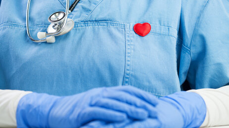 Bildet viser utsnitt av en sykepleier. På brystet har vedkommende et rødt hjerteformet emblem 