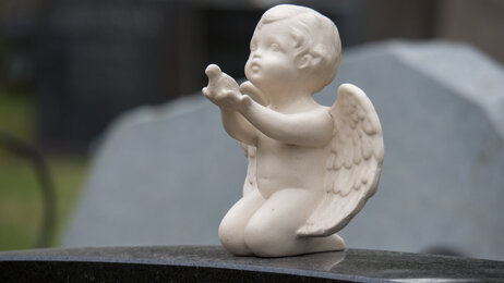 Bildet viser en gravstøtte pyntet med en hvit engel som strekker ut armene.