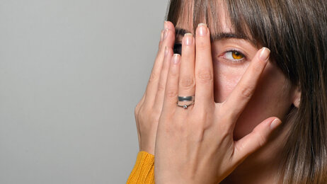Bildet viser en kvinne med hendene foran øynen, men som titter mellom to fingre
