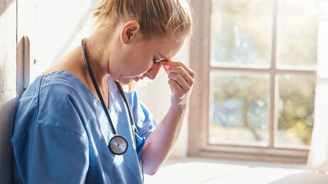 Bildet viser en sykepleier med fremoverbøyd hode. Hun er sliten og kniper seg over neseryggen