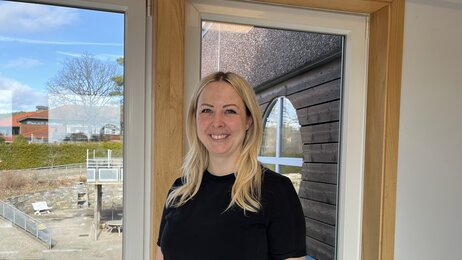 Bildet viser Helene Herlandsen. Hun står foran et vindu og smiler til kamera