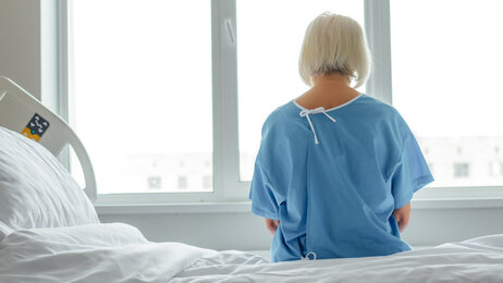 Bildet viser en pasient bakfra. Hun sitter på en sykehusseng og ser framfor seg.