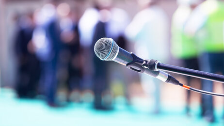Bilde av en mikrofon. I bakgrunnen kan man skimte tilhørere.