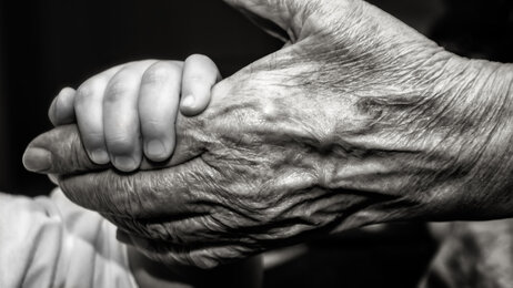 Bildet viser et lite barn som holder et gammelt menneske i hånden.