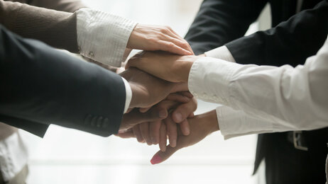 Bildet viser dresskledte mennesker som holder hendene oppå hverandre, som om de inngår en pakt.