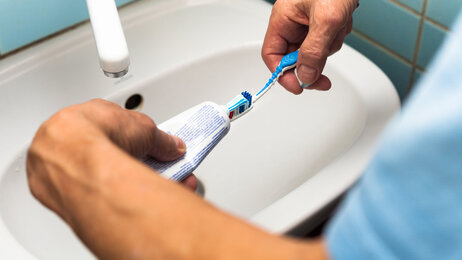 Bildet viser to hender som tar tannkrem på en tannbørste.