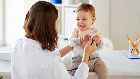 En blid baby sitter på et bord og blir undersøkt av en helsearbeider.