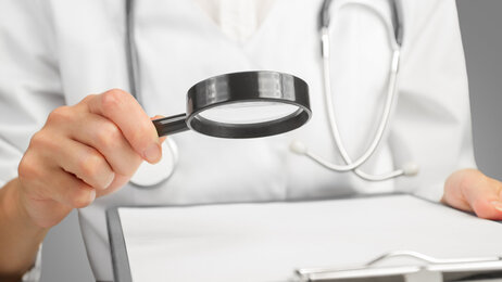 Bildet viser overkroppen til en sykepleier som holder et forstørrelsesglass