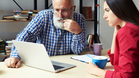 Ung jente viser en eldre mann noe på PC-en sin på et kontor