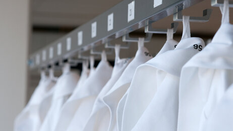 Bildet viser mange sykepleierantrekk som henger på rekke og rad.