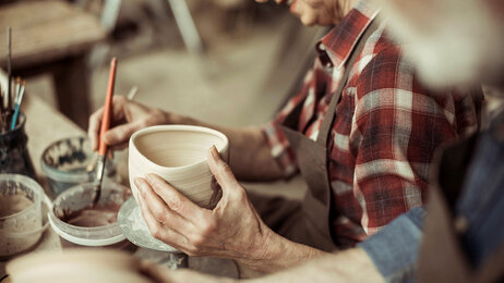 Bildet viser en eldre kvinne og en eldre mann som lager og dekorerer gjenstander i leire