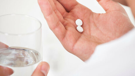 Sykepleier deler ut to piller og holder et glass vann.