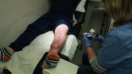 Bildet viser en sykepleier som utfører sårstell på en innsatt.