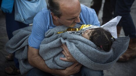 Bildet viser en mann med et lite barn inntullet i teppe i armene.