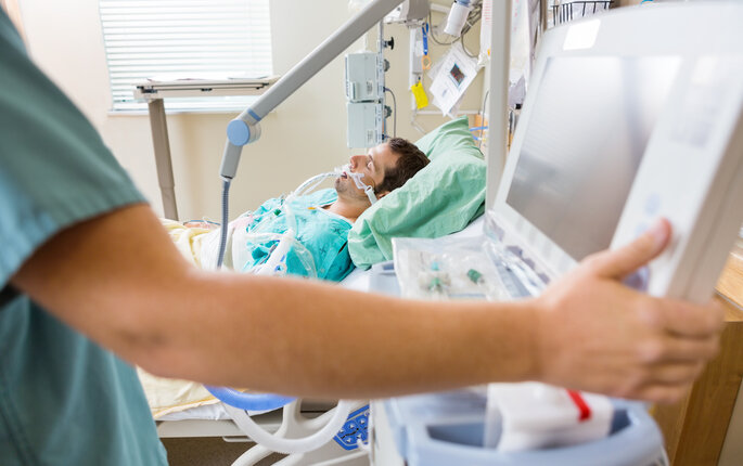 The photo shows nurse pressing monitor's button with male patient lying on bed in hospital