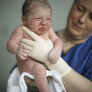 Bildet viser en jordmor som holder opp en nyfødt baby