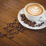 Bildet viser en kopp cappuccino og mange kaffebønner.
