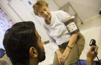 Mannlig sykepleier måler blodtrykket til eldre kvinne.