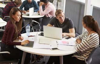 Bildet viser studenter som sitter rundt et bord og gjør gruppearbeid. 
