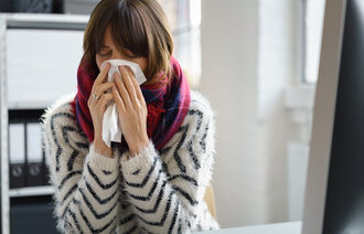 Kvinne med myk strikkegenser og mørkt glatt hår gjemmer ansiktet i et lommetørkle.  