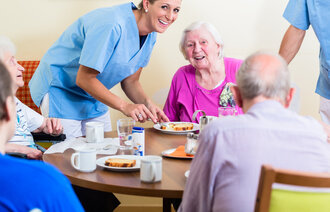 Bildet viser en smilende sykepleier sammen med fornøyde beboere ved et sykehjem.