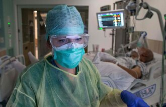 Bildet viser en sykepleier i smittevernutstyr og en pasient som blir overvåket i bakgrunnen.