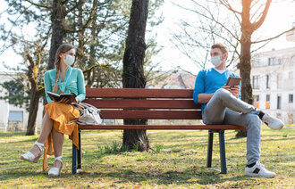 bildet viser et par på benk med avstand og munnbind