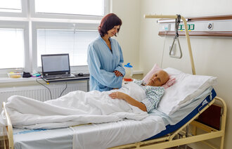 Bildet viser en kvinne som står ved sengen til en døende kvinnelig kreftpasient